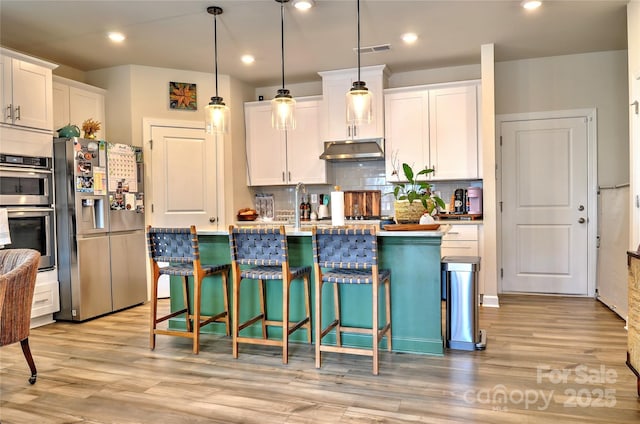 kitchen with light wood-type flooring, appliances with stainless steel finishes, pendant lighting, and white cabinetry