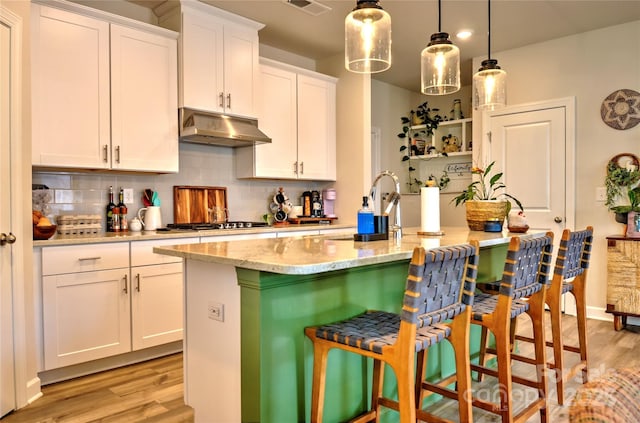 kitchen with a kitchen breakfast bar, a kitchen island with sink, hanging light fixtures, white cabinets, and backsplash