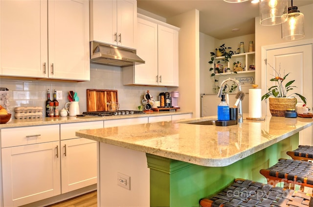 kitchen featuring white cabinetry, stainless steel gas stovetop, hanging light fixtures, light stone countertops, and a kitchen island with sink