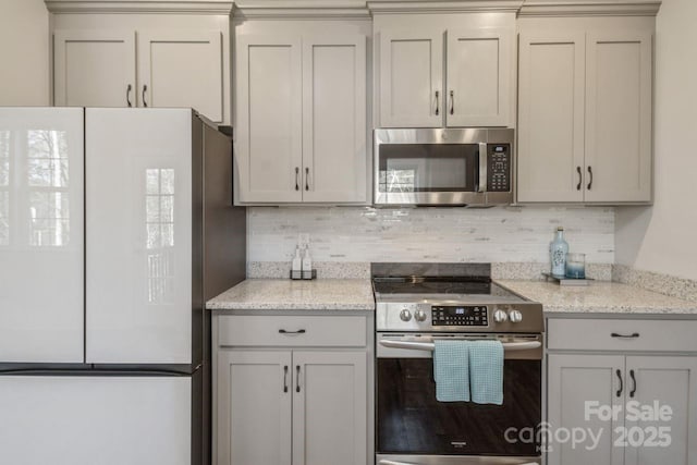 kitchen featuring stainless steel appliances, decorative backsplash, and light stone countertops