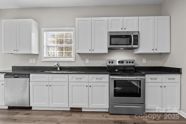 kitchen featuring hardwood / wood-style flooring, white cabinets, appliances with stainless steel finishes, and sink