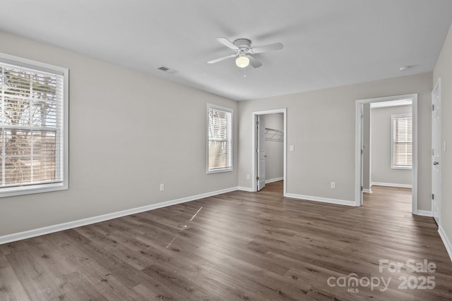 unfurnished bedroom with ceiling fan, a walk in closet, a closet, and dark hardwood / wood-style floors