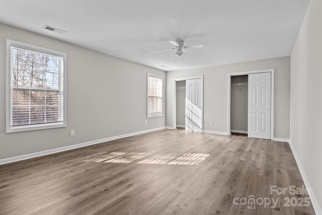 unfurnished bedroom with ceiling fan, two closets, and hardwood / wood-style flooring