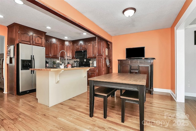 kitchen featuring stainless steel fridge, tasteful backsplash, light hardwood / wood-style floors, a textured ceiling, and a center island with sink