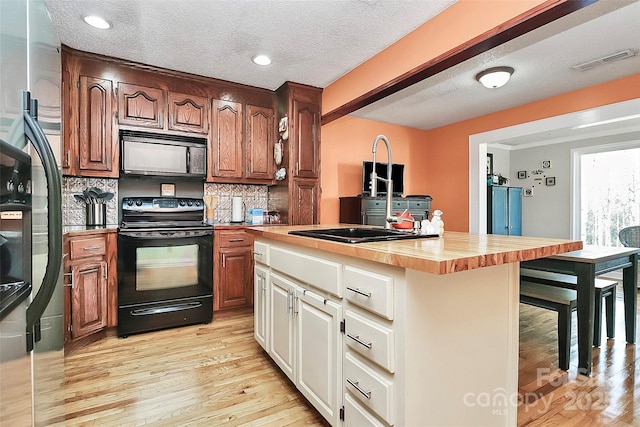 kitchen featuring a kitchen island, butcher block countertops, decorative backsplash, black appliances, and light hardwood / wood-style flooring