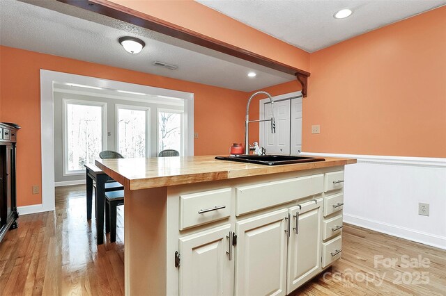 kitchen with butcher block counters, sink, cream cabinets, a textured ceiling, and light hardwood / wood-style flooring