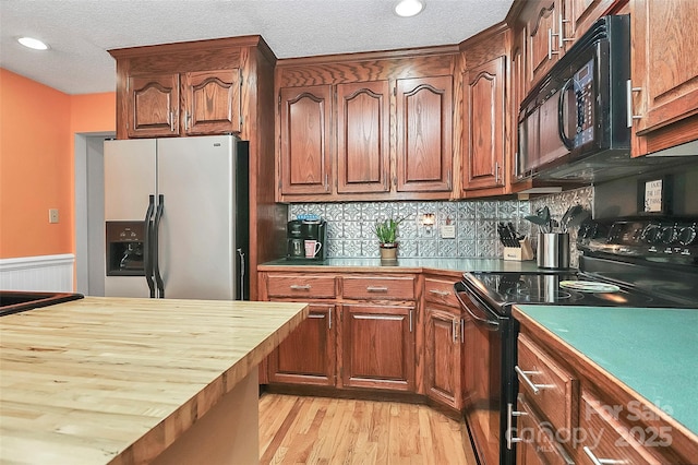 kitchen with tasteful backsplash, black appliances, a textured ceiling, wood counters, and light wood-type flooring