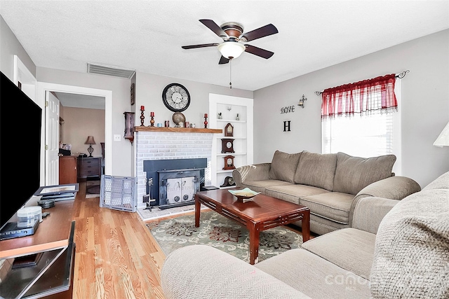 living room featuring built in features, ceiling fan, wood-type flooring, a textured ceiling, and a brick fireplace