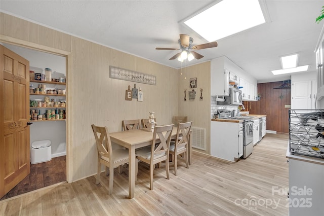 dining area with light wood-type flooring, ceiling fan, and wood walls