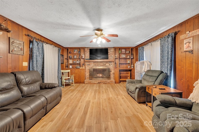 living room with a fireplace, built in features, ceiling fan, and wooden walls