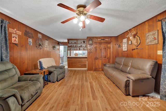 living room with wood walls, ceiling fan, and a textured ceiling