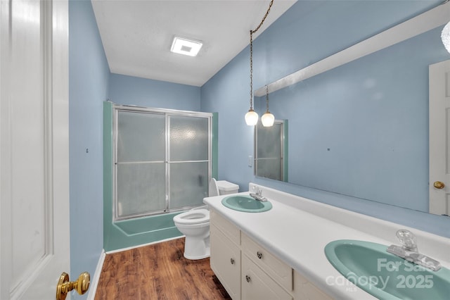 full bathroom with combined bath / shower with glass door, wood-type flooring, vanity, and toilet