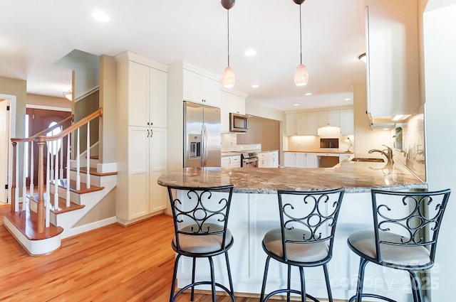 kitchen with sink, appliances with stainless steel finishes, white cabinetry, light stone countertops, and kitchen peninsula