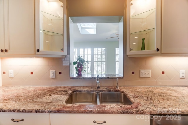 kitchen featuring light stone countertops, sink, decorative backsplash, and a skylight