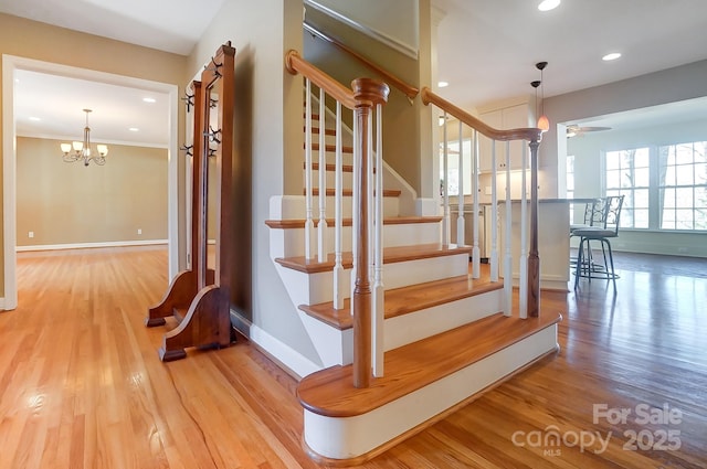 staircase featuring ornamental molding, wood-type flooring, and ceiling fan with notable chandelier