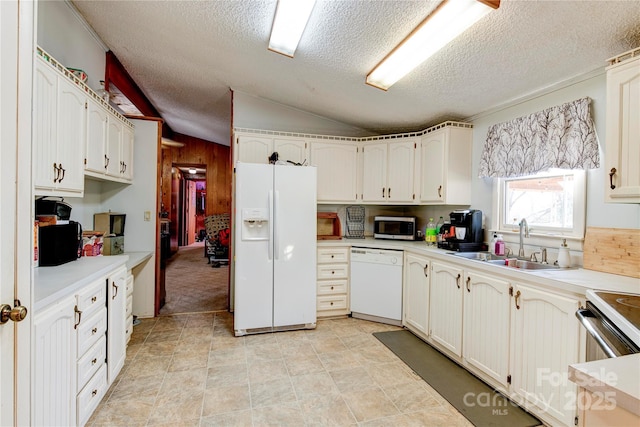 kitchen featuring white appliances, vaulted ceiling, sink, white cabinets, and wood walls