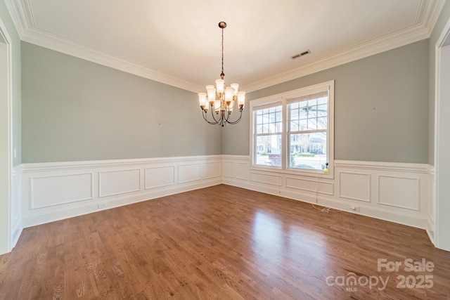 spare room featuring an inviting chandelier, ornamental molding, and hardwood / wood-style floors