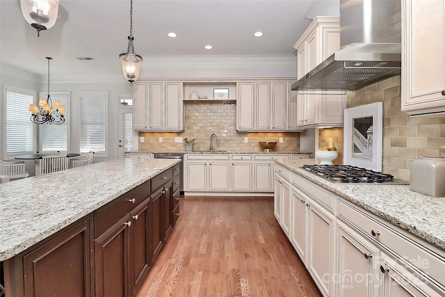 kitchen featuring tasteful backsplash, a notable chandelier, wall chimney range hood, pendant lighting, and light stone counters