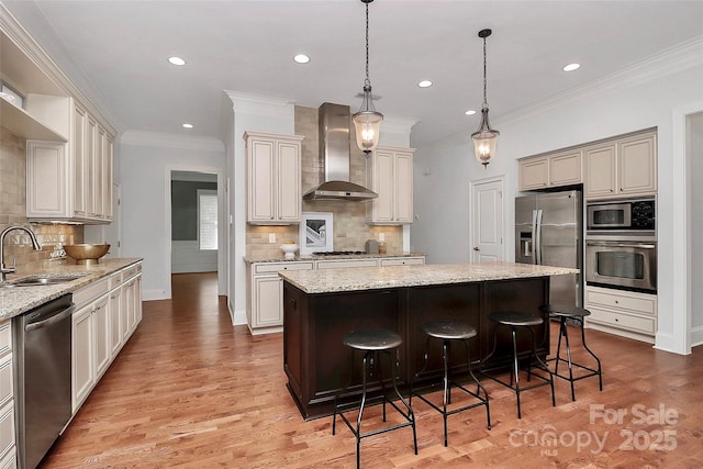 kitchen with wall chimney range hood, a kitchen island, sink, hanging light fixtures, and appliances with stainless steel finishes