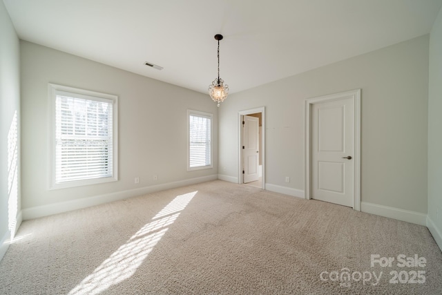 empty room with a wealth of natural light, light carpet, and an inviting chandelier