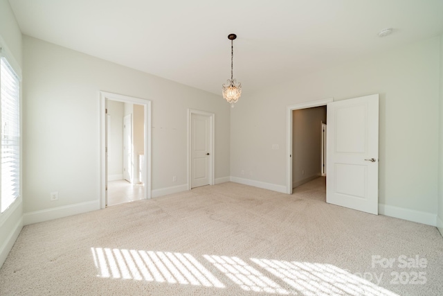 spare room featuring light colored carpet and a notable chandelier