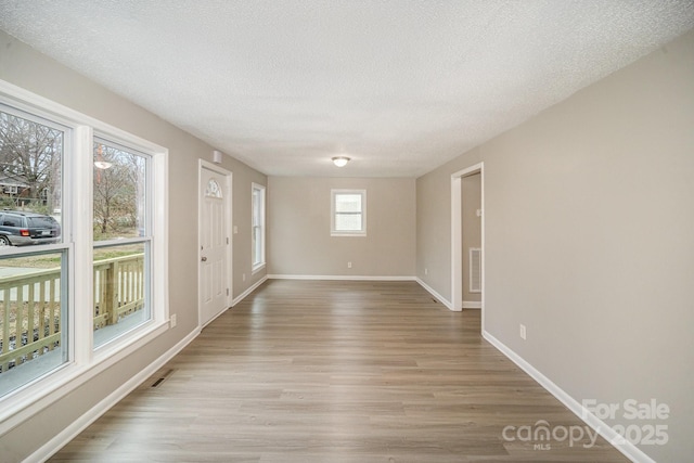 empty room with a textured ceiling and light hardwood / wood-style flooring