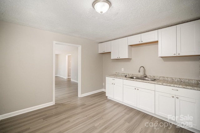 kitchen featuring sink, white cabinets, light stone counters, and a textured ceiling