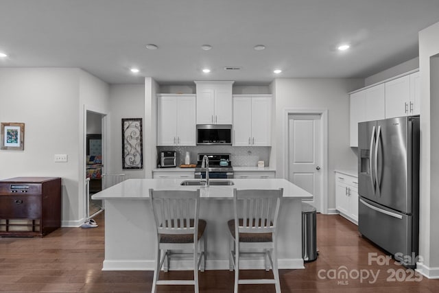 kitchen featuring appliances with stainless steel finishes, white cabinetry, a breakfast bar area, decorative backsplash, and a center island with sink