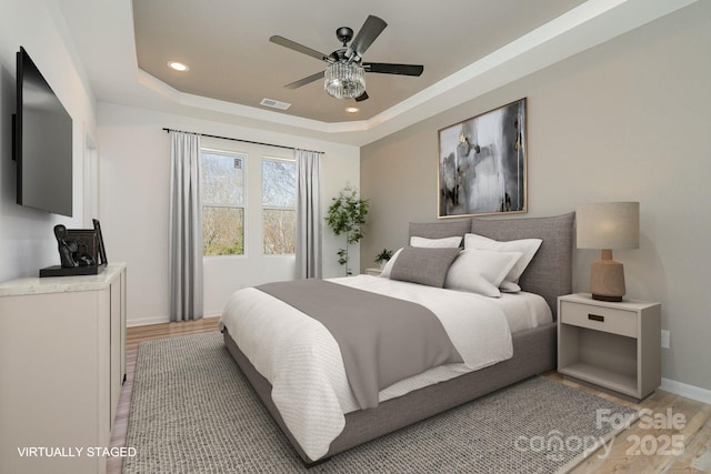 bedroom featuring ceiling fan, light wood-type flooring, and a tray ceiling