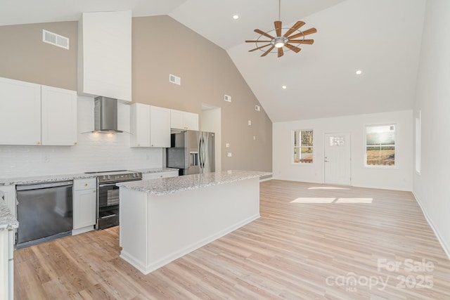 kitchen with a kitchen island, white cabinetry, light stone counters, stainless steel appliances, and wall chimney range hood