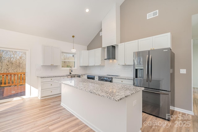 kitchen featuring wall chimney range hood, stainless steel fridge, a center island, white cabinets, and decorative light fixtures