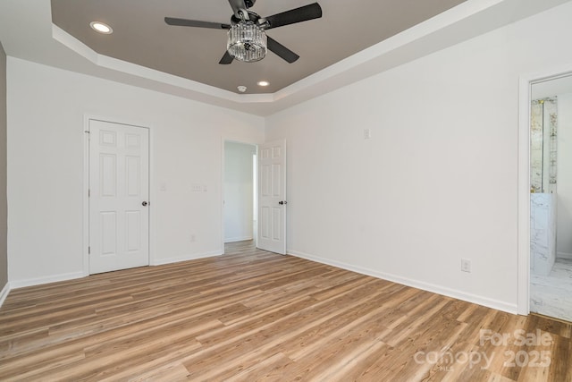 unfurnished bedroom featuring ceiling fan, light hardwood / wood-style flooring, ensuite bath, and a tray ceiling