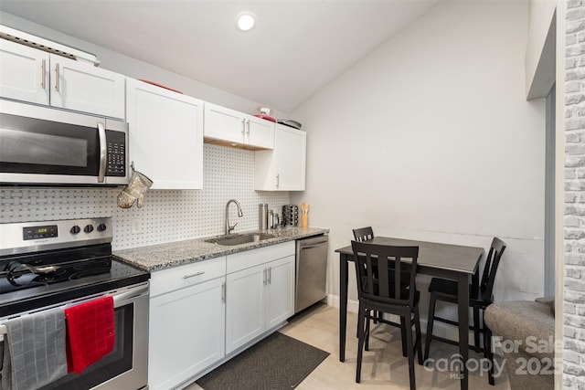 kitchen with lofted ceiling, sink, white cabinetry, light stone countertops, and stainless steel appliances