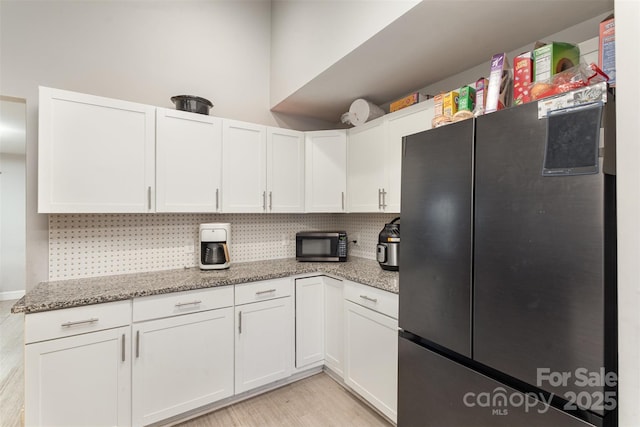 kitchen with light stone counters, white cabinets, and stainless steel refrigerator