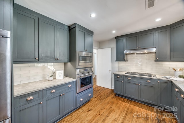 kitchen featuring decorative backsplash, light stone counters, light hardwood / wood-style flooring, and stainless steel appliances