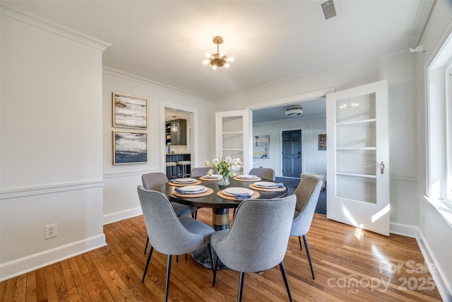 dining space with wood-type flooring, built in features, an inviting chandelier, and ornamental molding