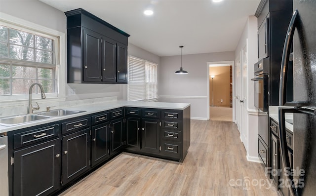 kitchen with black appliances, decorative light fixtures, light hardwood / wood-style floors, sink, and kitchen peninsula