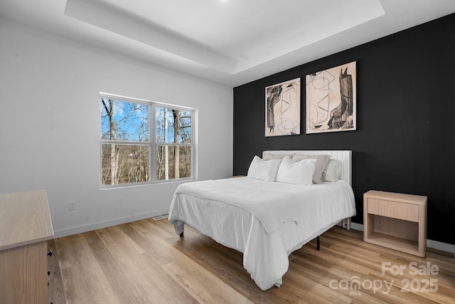 bedroom with a raised ceiling and light hardwood / wood-style flooring