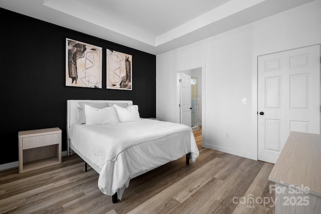 bedroom featuring hardwood / wood-style floors, a tray ceiling, and ensuite bathroom