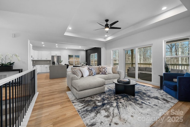 living room with ceiling fan, light hardwood / wood-style floors, and a tray ceiling