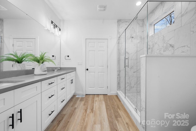 bathroom with wood-type flooring, a shower with door, and vanity