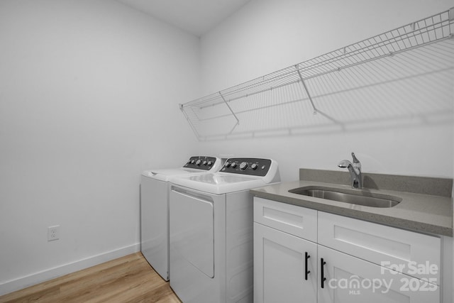 clothes washing area with washer and dryer, sink, light hardwood / wood-style floors, and cabinets