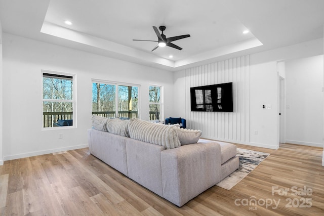 living room featuring light wood-type flooring, ceiling fan, and a tray ceiling