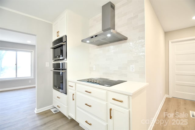 kitchen featuring tasteful backsplash, white cabinets, wall chimney range hood, and light wood-type flooring