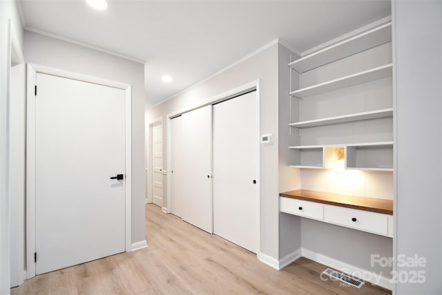 interior space with a closet, light hardwood / wood-style flooring, built in desk, and ornamental molding