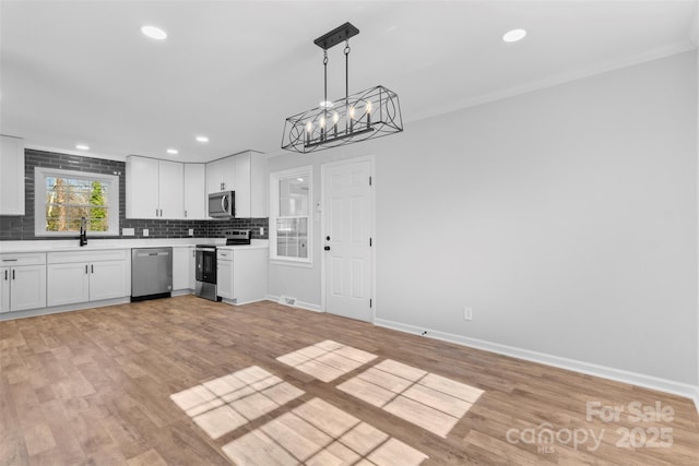 kitchen with white cabinetry, tasteful backsplash, light hardwood / wood-style flooring, pendant lighting, and appliances with stainless steel finishes