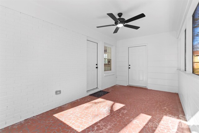 unfurnished room with ceiling fan and brick wall