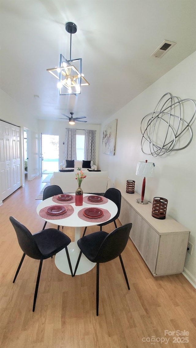 dining room with light wood-type flooring and ceiling fan with notable chandelier