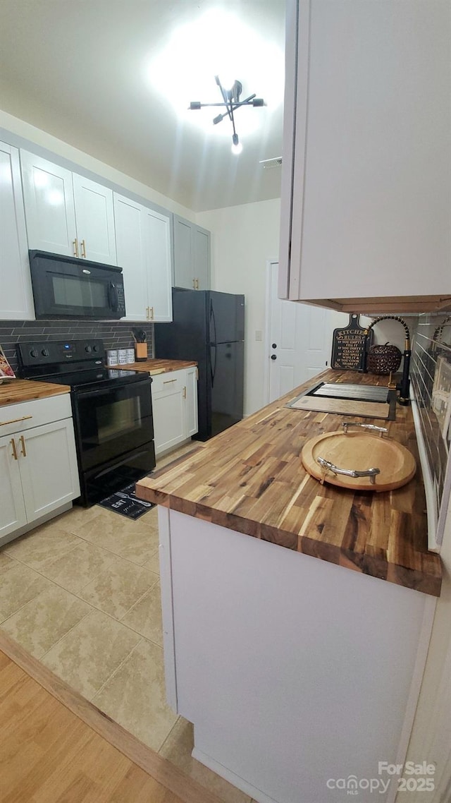 kitchen with light tile patterned floors, butcher block countertops, white cabinets, and black appliances