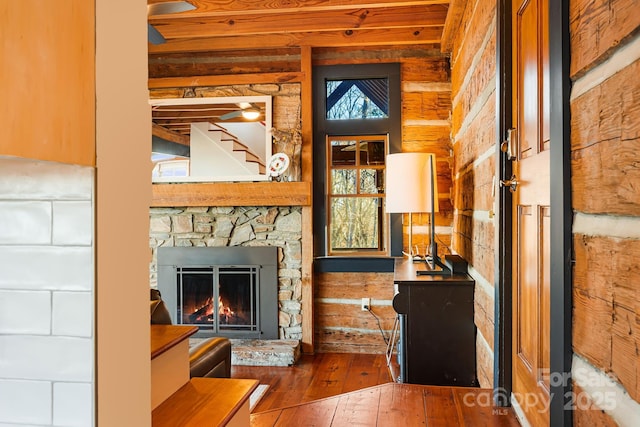 living room featuring log walls, hardwood / wood-style flooring, wooden ceiling, and a stone fireplace